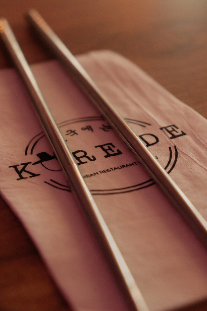 Close-up of metal chopsticks resting on a napkin with Korean restaurant logo.