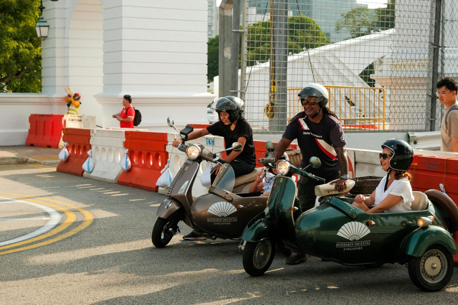 Tourists riding vintage sidecar scooters enjoy a sunny day near a historic building in Singapore.