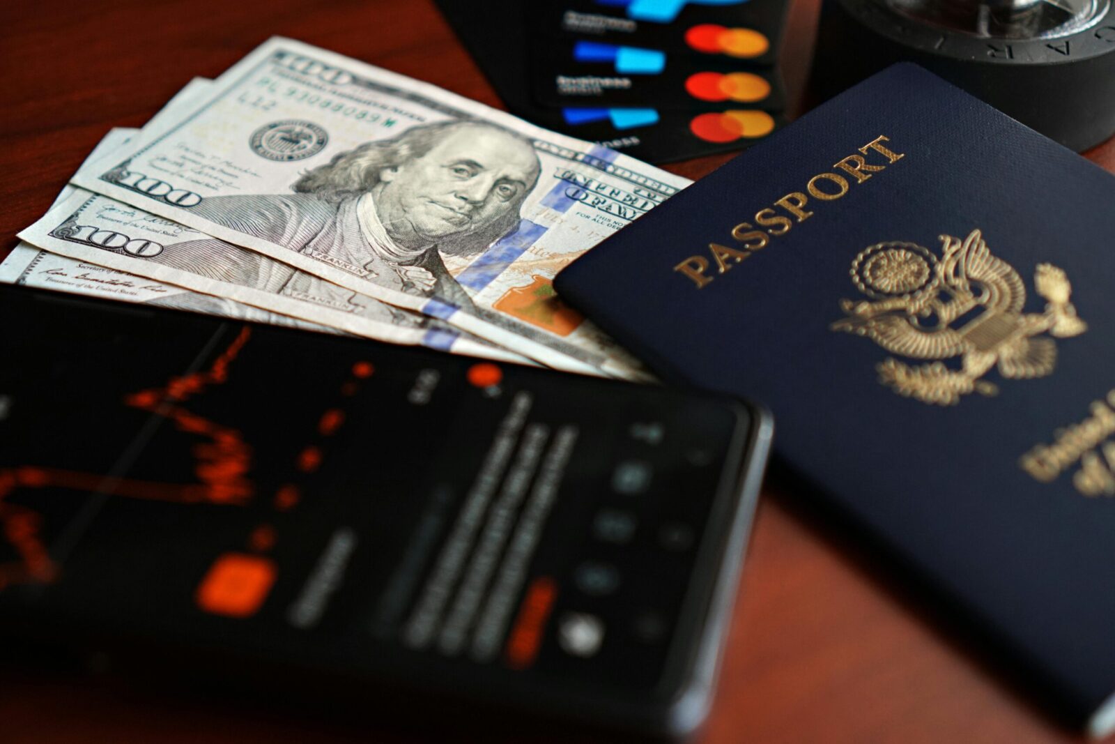 A flat lay of travel essentials including a passport, US currency, and credit cards on a table.